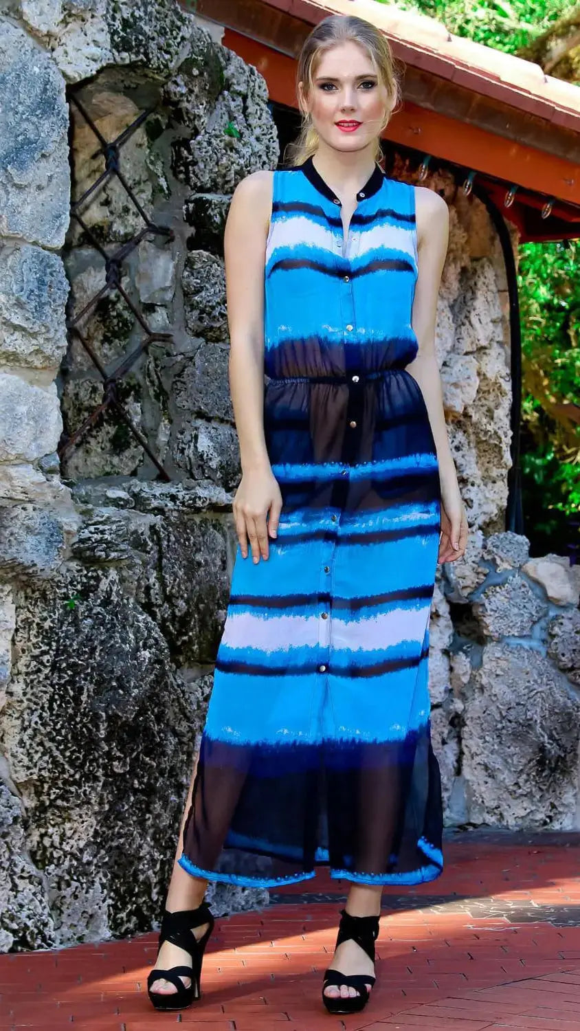 A woman stands outdoors by a stone wall, wearing the lamodaclothings Front Button Beach or Swim Cover Up Sheer Dress. She pairs it with black wedge sandals; her blonde hair is tied back and the background features greenery and a red-tiled roof.