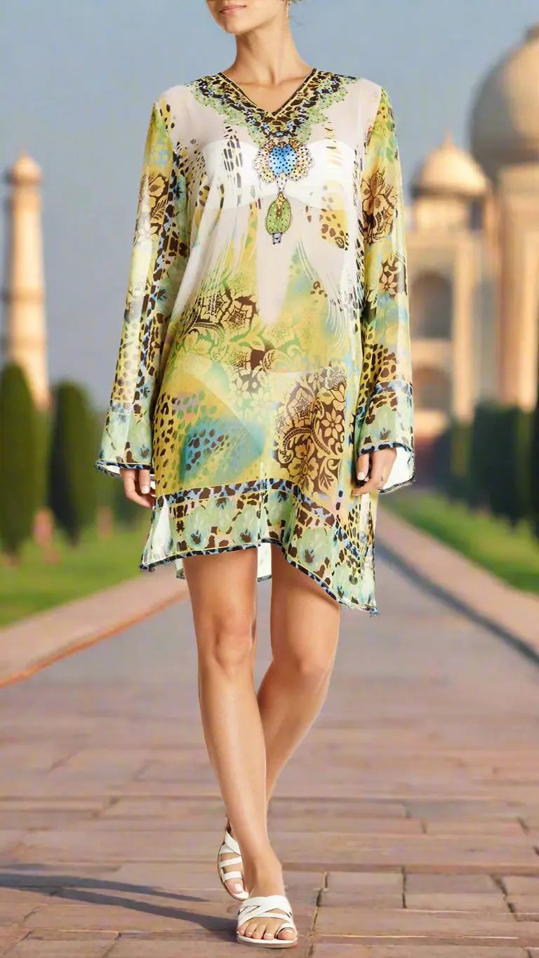 A woman wears the Lamodaclothing Jungle Print Tunic, a flowy sheer dress with green, yellow, and brown designs—perfect for a tropical vacation—as she stands in white sandals before the softly blurred Taj Mahal.