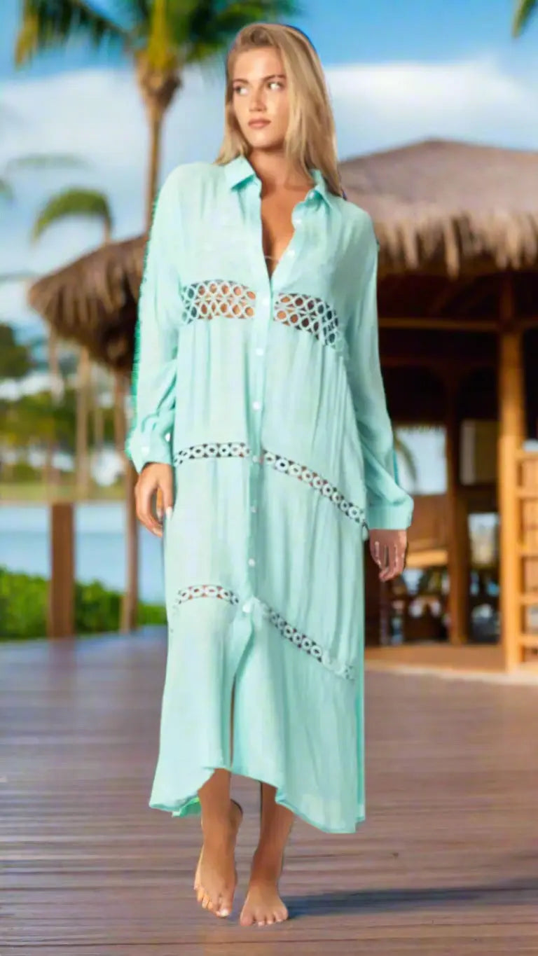 A woman with long blonde hair wears the La Moda Clothing Loose Long Sleeve Shirt Dress Swimsuit Cover Up in light turquoise, walking barefoot on a wooden deck by thatched roofs, palm trees, and water under a sunny sky.