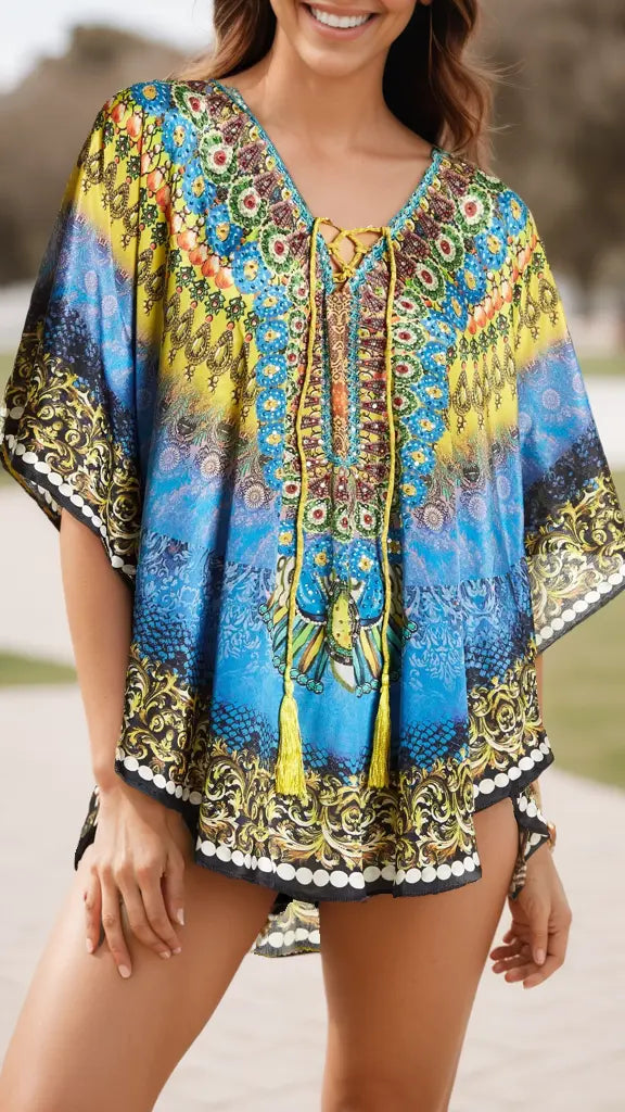 A woman smiles outdoors in the lamodaclothings Relaxed Short Kaftan Cover-Up, a colorful, loose-fitting style with blue, yellow, and green patterns and tassel accents. The blurred background highlights her vibrant look.