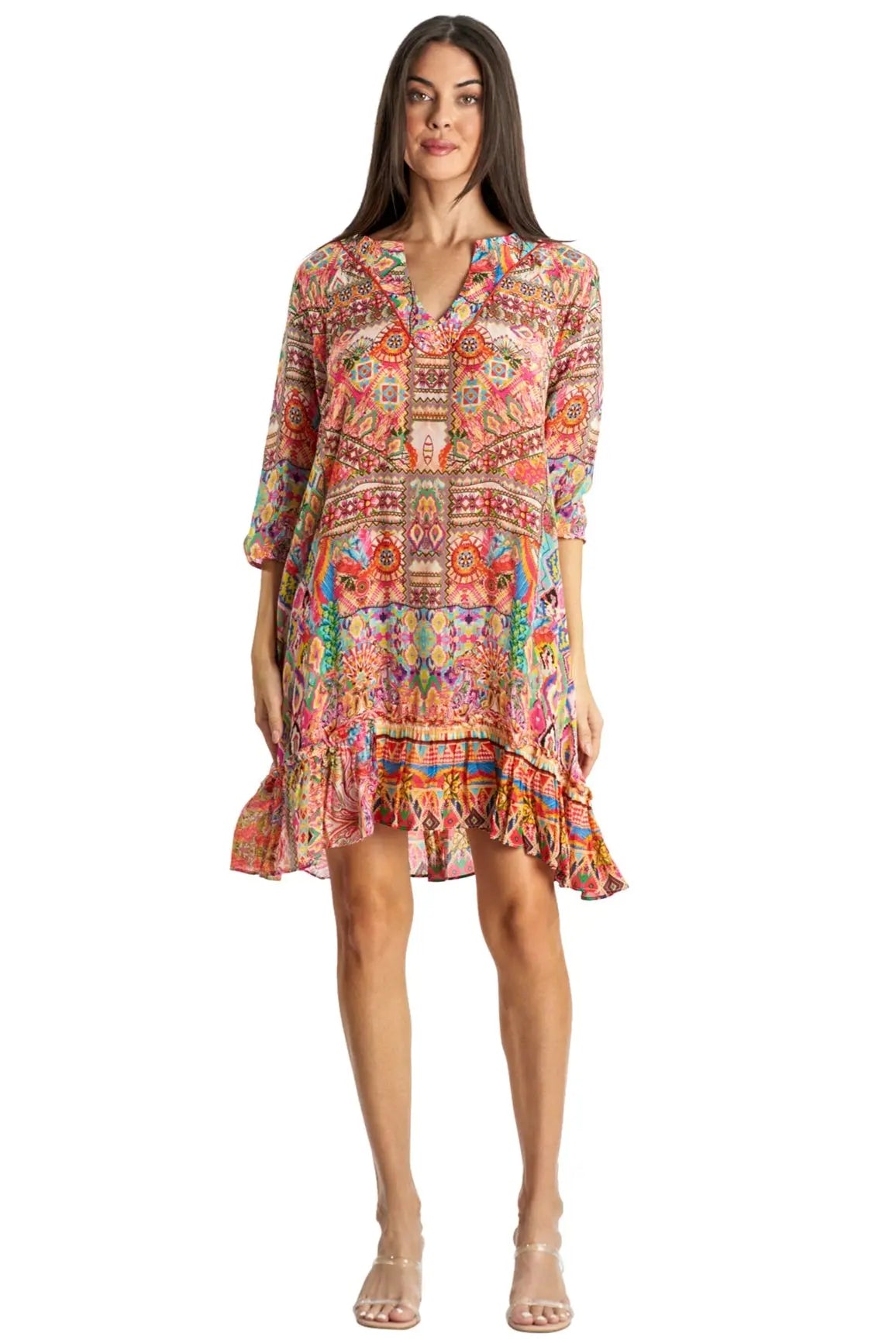 A woman stands facing forward in a vibrant, patterned Short Dress by La Moda Clothing. With long sleeves, a ruffled hem, and clear high-heeled sandals, this chic piece adds versatility to any wardrobe.