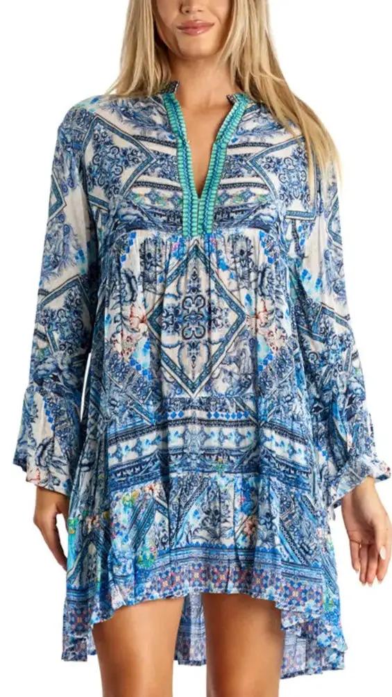 A woman wears La Moda Clothings Spring Dresses—a loose, long-sleeved design featuring blue and white mandala and paisley prints, turquoise bead details on the V-neckline, and a slightly flared flowy skirt made from lightweight fabric.