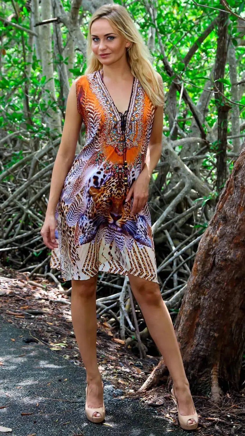 A woman with long blonde hair stands outdoors among tree branches, wearing the lamodaclothings Tunic-Style Cover-Up Mini Dress with a wildlife print and beige peep-toe heels, posing with one hand on her hip.