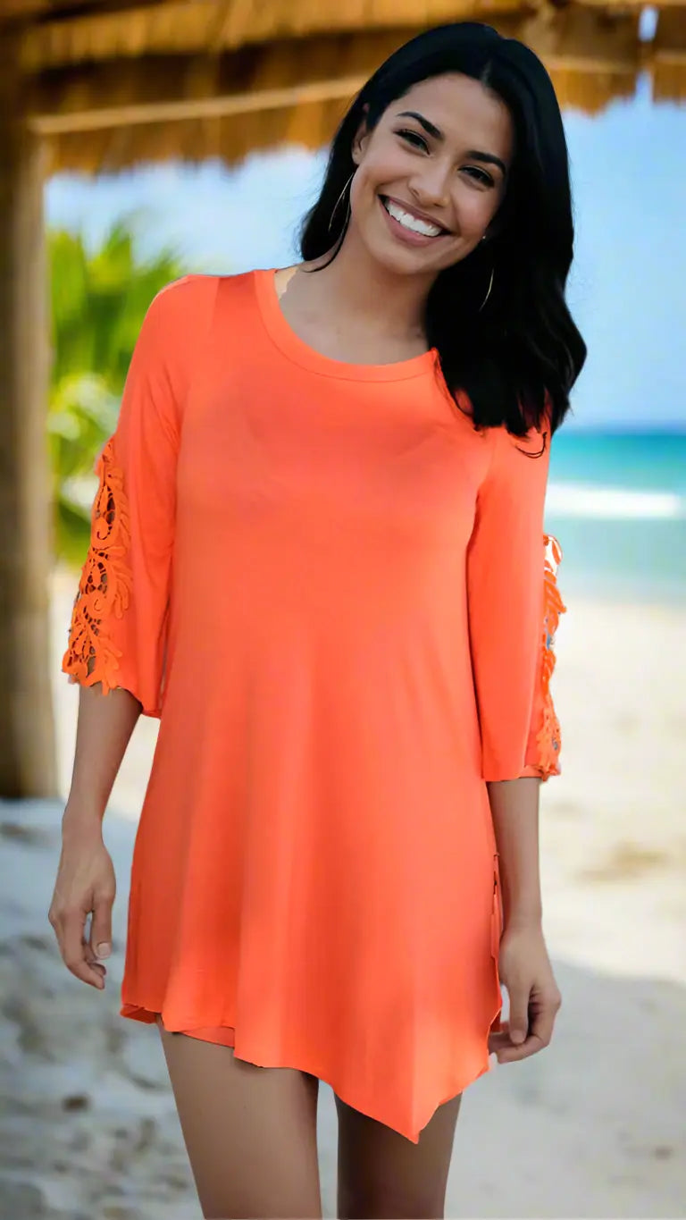 A woman with long dark hair stands on a sunny beach, smiling in the Lamodaclothing Knitted Beach Tunic Cover-Up. Palm trees, blue sky, and ocean waves complete the tropical background.