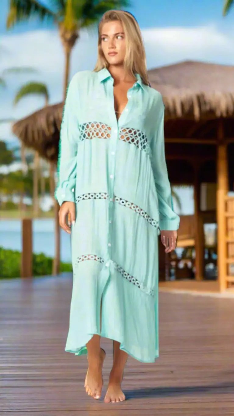 A woman with long blonde hair wears the La Moda Clothing Loose Long Sleeve Shirt Dress Swimsuit Cover Up in light turquoise, walking barefoot on a wooden deck by thatched roofs, palm trees, and water under a sunny sky.
