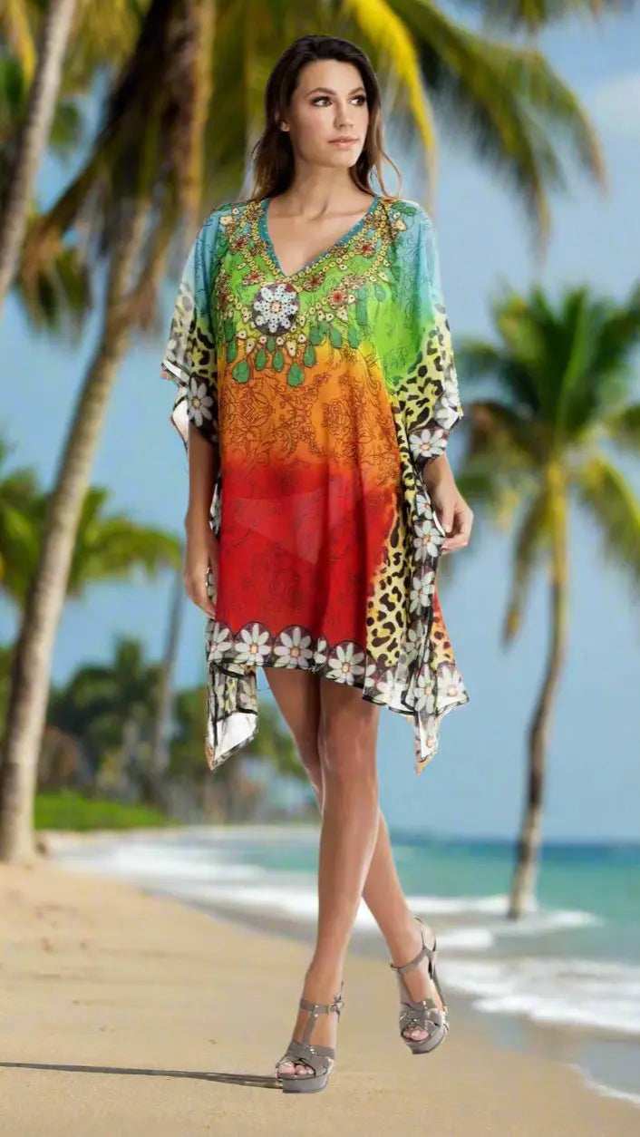 A woman wears the lamodaclothings Multi Color Sheer Kaftan/Cover Up, featuring floral and animal prints, as she strolls barefoot along a sandy beach with palm trees and ocean under a blue sky, her brown hair loose and smiling ahead.