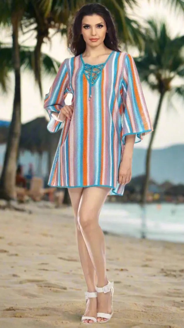 A woman stands on a sandy tropical beach with palm trees, wearing the Lamodaclothing Multi-Color Stripe Pattern Beach Cover-Up Tunic and white heeled sandals. The ocean shimmers serenely in the background.
