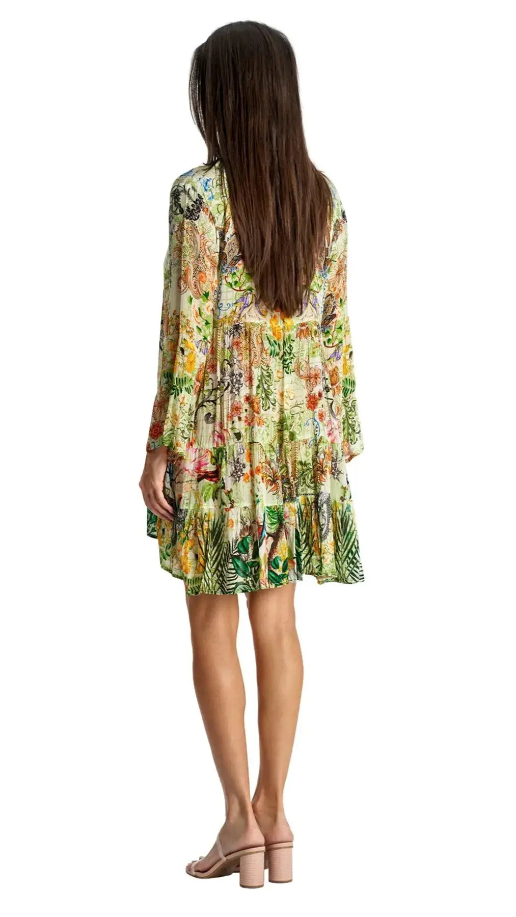 A woman with long brown hair faces away, showcasing the back of the La Moda Clothing Mini Dress for beach resort & cruise—a flowy, multicolored floral mini dress with long sleeves and ruffled hem, paired with nude block-heeled sandals.