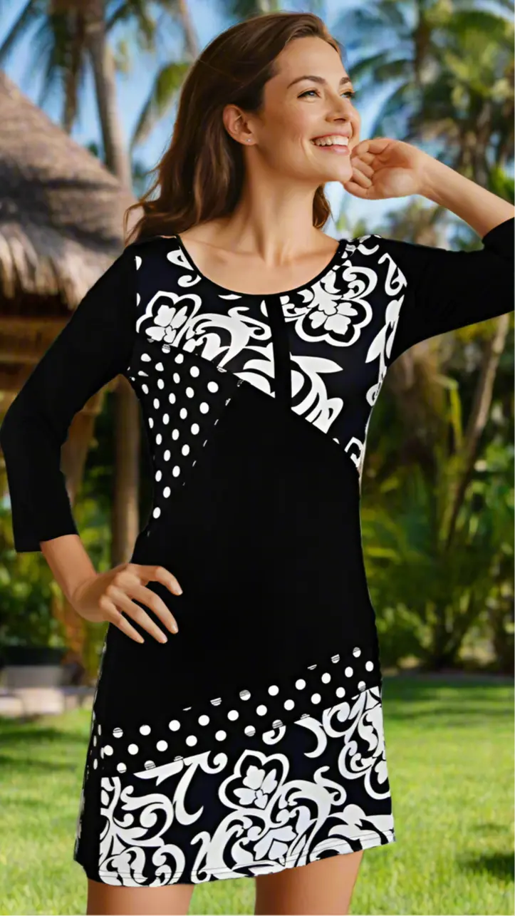 A smiling woman with medium-length brown hair models the lamodaclothings Resortwear Beachwear & Cruisewear Knit Dress, featuring bold white floral and polka dot patterns, standing outdoors with lush greenery and a thatched hut in the background.