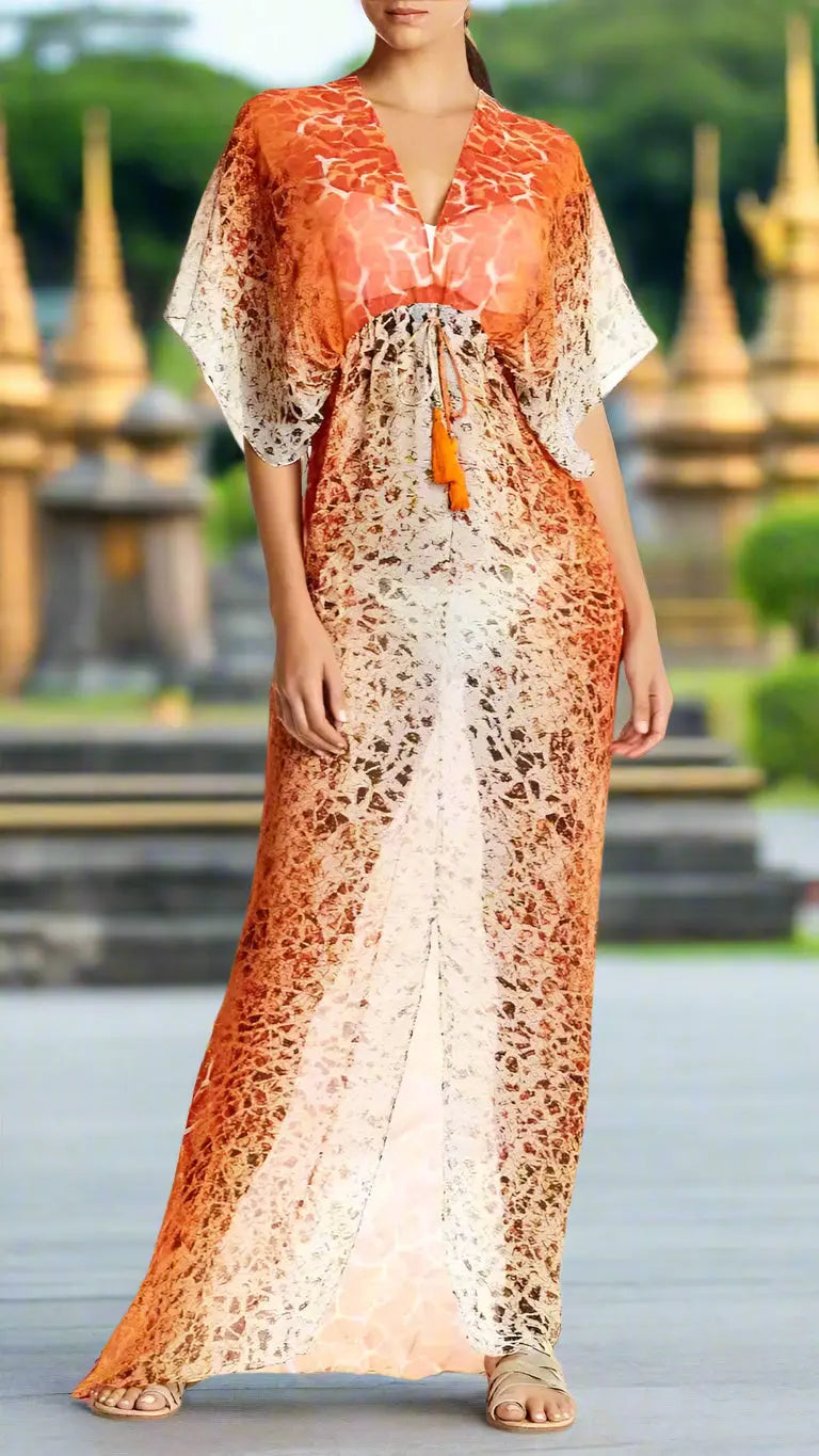 A woman wears the lamodaclothings Sheer Long Kaftan Beachwear Cover Up, a flowing orange and cream patterned dress with wide sleeves, V-neck, waist tie with orange tassels, and flat sandals outdoors near blurred golden pagodas.